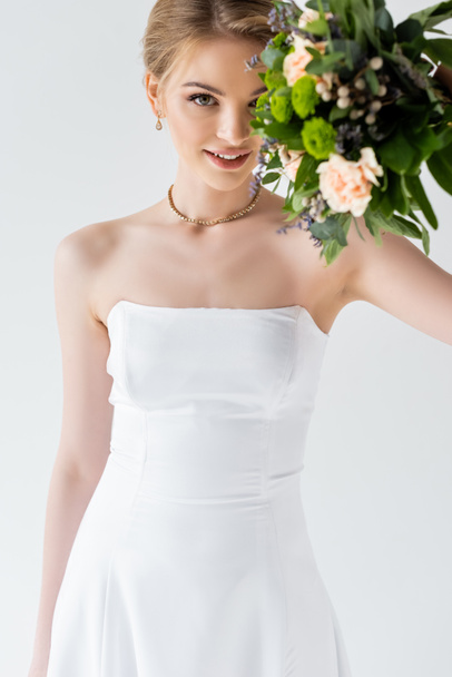 jong en gelukkig bruid in elegante trouwjurk met bloemen geïsoleerd op wit  - Foto, afbeelding