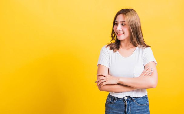 Asian Thai happy portrait beautiful cute young woman standing wear t-shirt her smile confidence with crossed arms looking to side up isolated, studio shot on yellow background and copy space - Photo, image