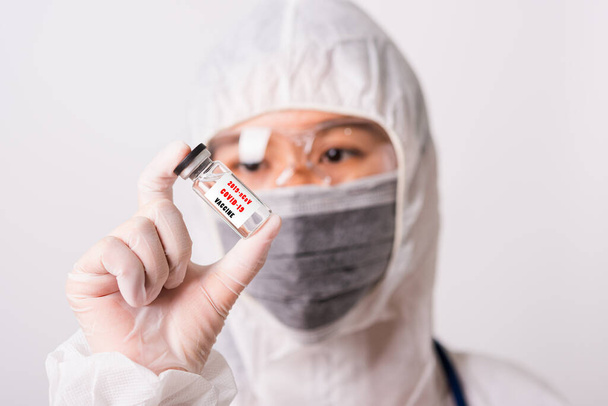 Asian female woman doctor or nurse in PPE uniform and gloves wearing face mask protective in laboratory holding medicine vial coronavirus vaccine bottle and on bottle has "COVID-19 VACCINE" text label - Fotoğraf, Görsel