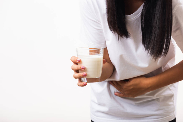 Closeup young woman intolerant use hand holding glass milk she is bad stomach ache she has bad lactose intolerance unhealthy problem with dairy food products, studio shot isolated on white background - 写真・画像
