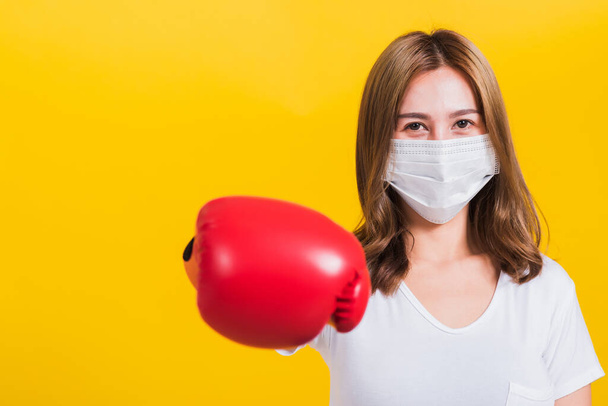 Portrait Asian Thai beautiful happy young woman wearing mask protection and boxing gloves her get ready for Coronavirus fighting against, studio shot isolated on yellow background, with copy space - Foto, immagini