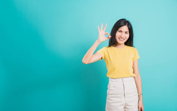 Portrait Asian beautiful young woman standing, She made finger OK symbol sign to agree and looking at camera, shoot photo in studio on blue background, There was copy space - Foto, immagini