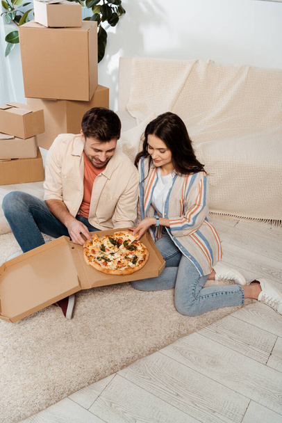 Gülümseyen adam yeni evinde kız arkadaşının yanında pizza tutuyor. - Fotoğraf, Görsel