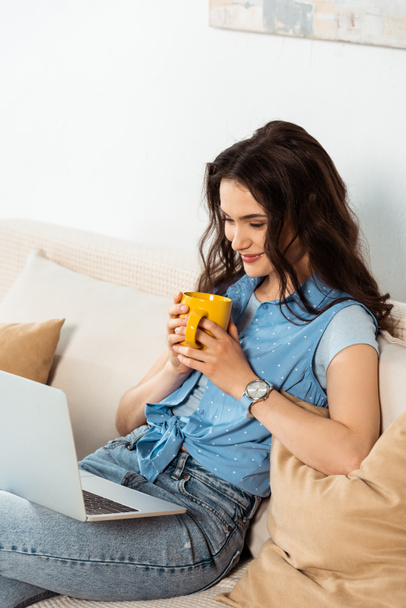 Beautiful smiling woman holding coffee cup and using laptop at home  - Foto, Imagem