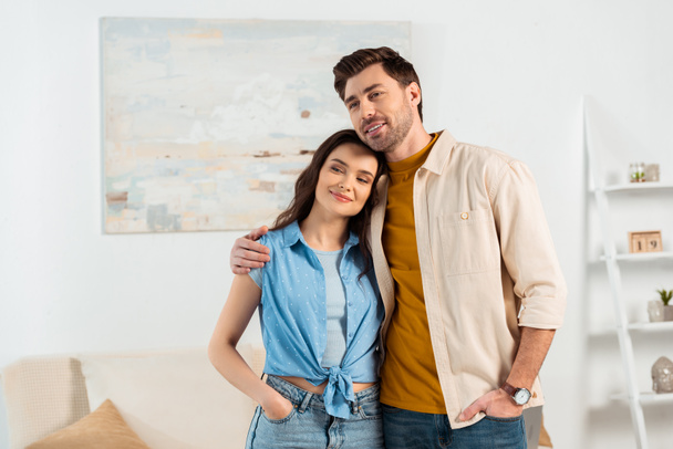 Giovane coppia sorridente via mentre abbraccia in soggiorno - Foto, immagini