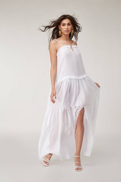 Beautiful woman fashion model makeup brunette hair perfect body shape tanned skin wear clothes summer collection organic long white silk dress stylish sandals shoes, accessory jewelry earrings date. - 写真・画像