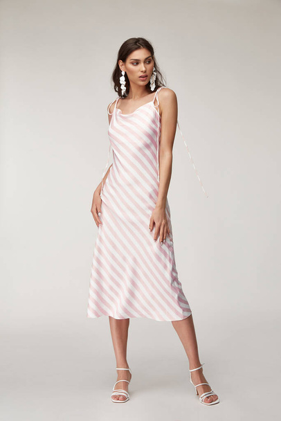 Sexy fashion model beautiful woman pretty face natural makeup, tanned skin body  wear summer collection clothes style romantic date walk casual trendy light silk in white pink stripes dress earrings. - Φωτογραφία, εικόνα