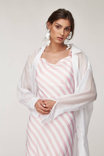 Sexy fashion model beautiful woman pretty face makeup, tanned skin wear summer collection clothes style for romantic date walk trendy light silk in white pink stripes long dress white shirt earrings. - Φωτογραφία, εικόνα