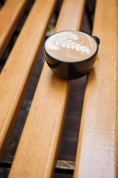 Cup of cappuccino with a pattern on a wooden bench. - Photo, image