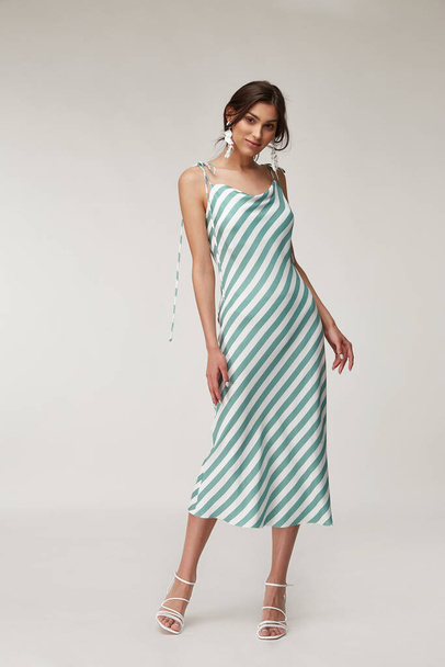 Fashion pretty woman beautiful makeup perfect body shape tanned skin wear clothes summer collection organic textile blue stripes silk dress stylish sandals shoes, accessory jewelry earrings romantic. - Foto, afbeelding