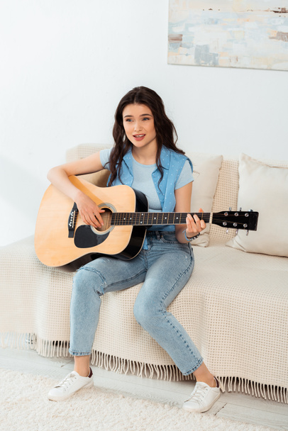 Beautiful woman singing and playing acoustic guitar at home  - Foto, afbeelding