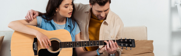Vista panorámica del hombre enseñando a su novia a tocar la guitarra acústica
  - Foto, imagen