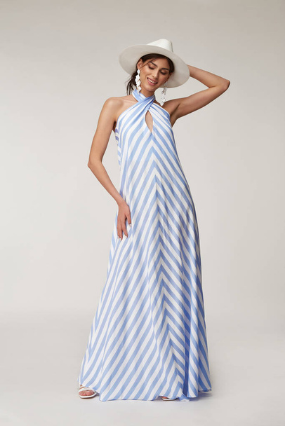Sexy fashion model beautiful woman pretty face natural makeup tan skin body  wear summer collection clothes style romantic date walk light silk in white blue stripes long dress earrings accessory hat. - Fotó, kép