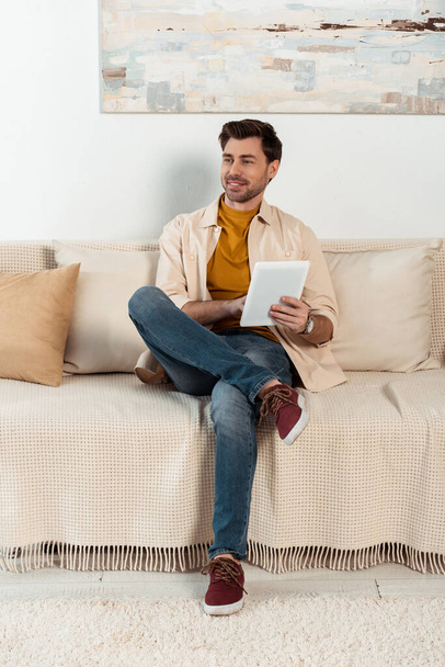 Handsome smiling man using digital tablet on couch at home  - Photo, Image