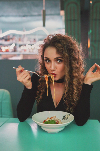 Cute girl with curly hair eating pasta in a restaurant. - Φωτογραφία, εικόνα