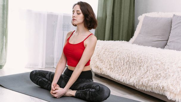 Mujer bonita practica yoga en un fondo interior casero. Relajación y meditación en posición de loto. - Foto, Imagen