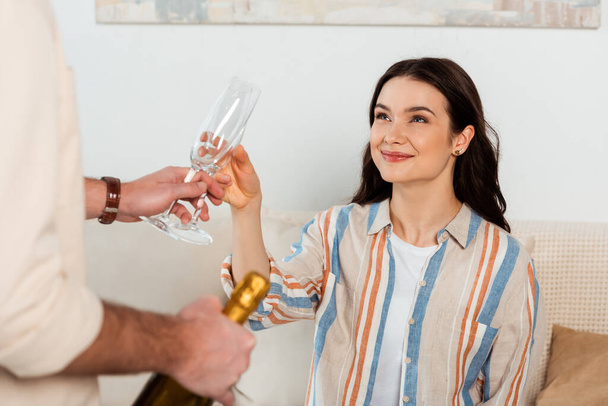 Selective focus of smiling woman holding glass of champagne near boyfriend with bottle at home  - 写真・画像