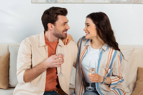 Happy woman holding glass of champagne and embracing boyfriend at home  - Photo, Image