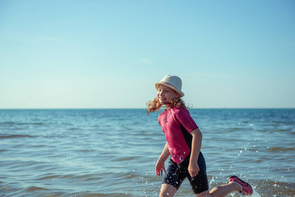 Happy pretty teen girl in neoprene swimingsuit  playing and running in Baltic sea - Photo, Image