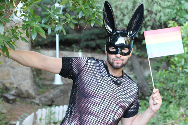 close-up portret van knappe jonge man in gay trots kostuum met konijn masker en lgbt vlag op straat - Foto, afbeelding