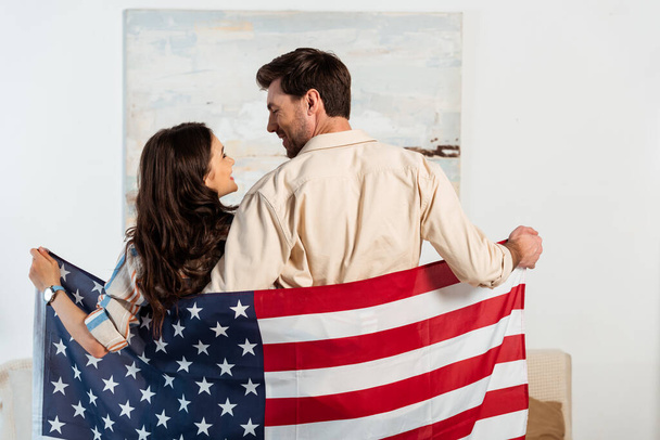 Visszapillantás fiatal pár mosolyog egymásra, miközben tartja amerikai zászló otthon  - Fotó, kép