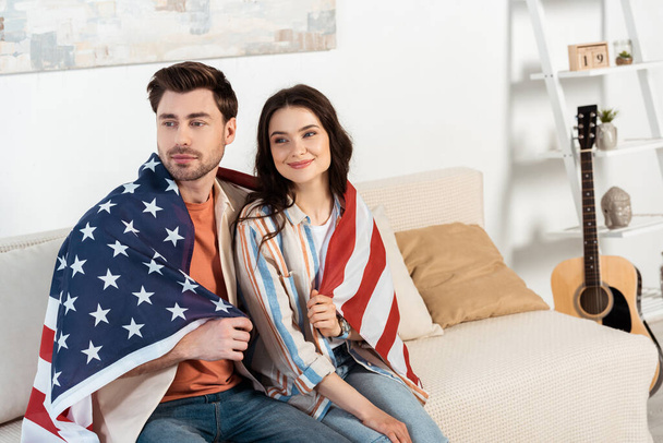 Amerikan bayrağına sarılı genç çift evdeki kanepede oturuyor.  - Fotoğraf, Görsel