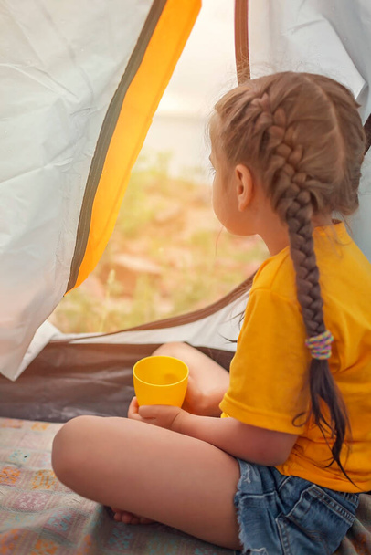 Fuga di famiglia locale. Bambino seduto nella tenda del campeggio al campeggio e guardando il tramonto, stile di vita attivo sano, sicuro soggiorno estivo dopo l'isolamento - Foto, immagini