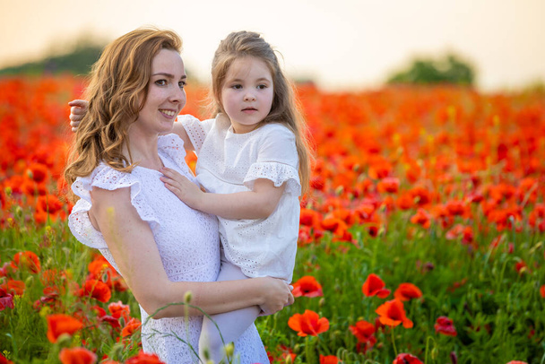 Beautiful mother and her daughter in spring poppy flower field in Czech republic - Photo, Image