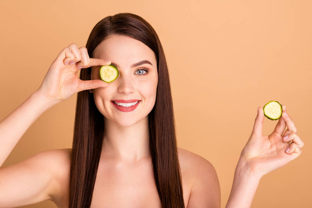 Close up photo of charming positive girlish girl hold cucumber slices cover close eyes want try new natural skin face treatment to have fresh body isolated over beige color background - Foto, Bild