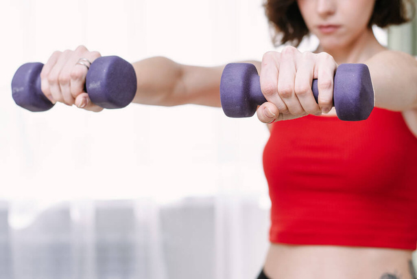 Lovely woman goes in for sports with dumbbells at home. Determined woman losing weight at home and exercising with dumbbells. Sport and recreation concept. - Photo, Image