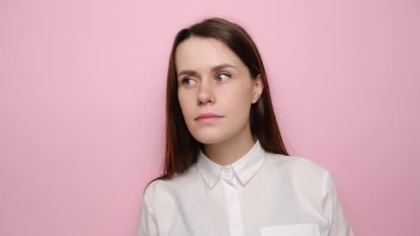 Smiling brunette woman looking aside try to hear you with hand at ear overhears secrets, isolated on pink wall background studio. Young girl in white shirt. People sincere emotions lifestyle concept - Кадры, видео