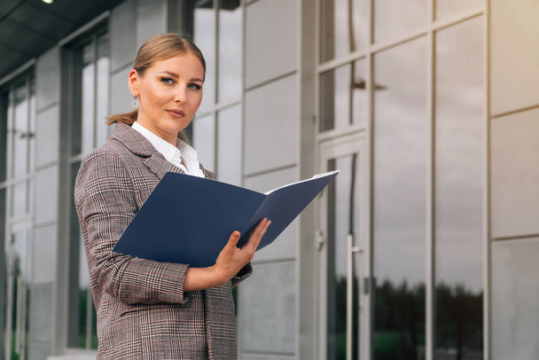 Stylish elegant woman of European appearance holds a folder with documents. The concept of a business lady against the background of the business center - Foto, afbeelding