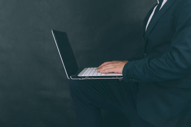 Businessman with jacket on a dark background with a laptop in his hands - Foto, Imagem