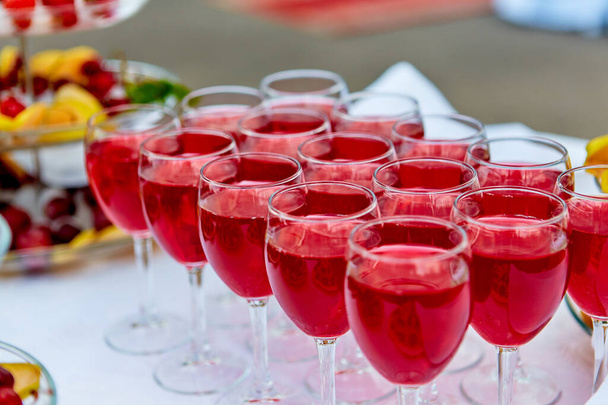 A row of glasses with red drinks, juice, champagne or wine at a party. Catering. Glassware on the table with a white tablecloth. Festive buffet for the holiday - Фото, изображение