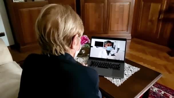Starsza kobieta w domowej masce odmładzającej w czasach koronawirusów podczas rozmowy wideo z lekarzem - Materiał filmowy, wideo