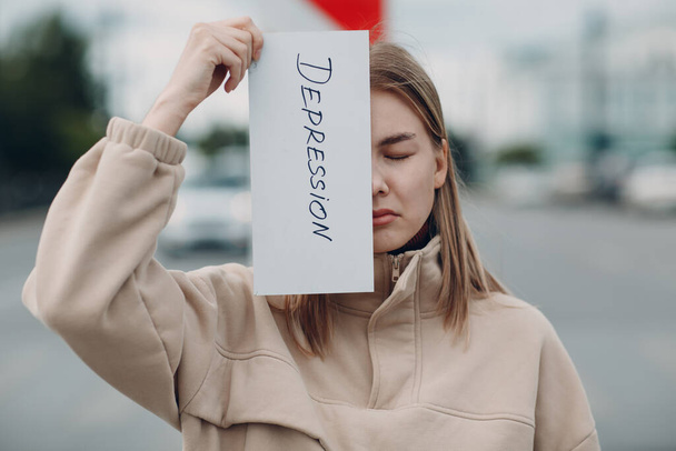 Woman holding white sheet paper labeled word Depression in hand. - Φωτογραφία, εικόνα
