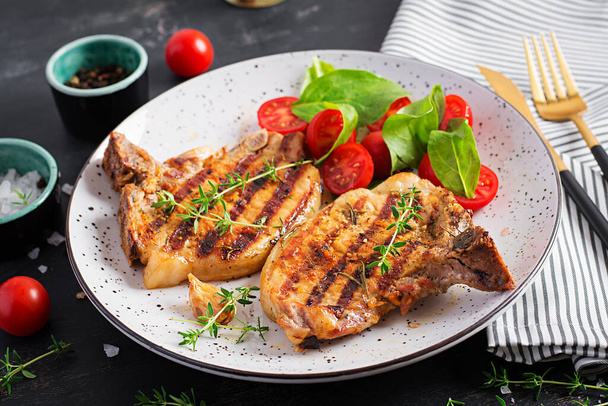 Grilled pork steaks and salad with tomatoes in plate on dark background. - Photo, Image