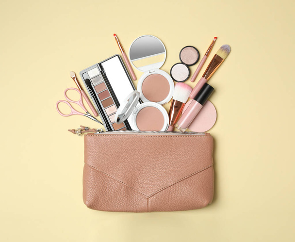Cosmetic bag with makeup products and beauty accessories on beige background, flat lay - Φωτογραφία, εικόνα