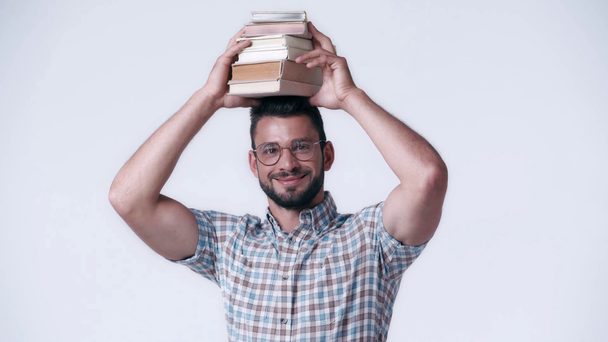 χαμογελαστός σπασίκλας με γυαλιά και καρό πουκάμισο με βιβλία στο κεφάλι απομονωμένα σε λευκό - Πλάνα, βίντεο