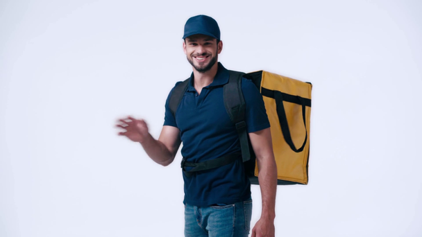 smiling delivery man walking with backpack and waving hand isolated on white - Кадры, видео