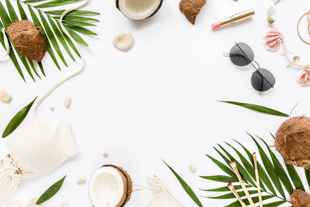 Feminine beige swimsuit beach accessories, tropical palm leaf branches, coconuts on white background. Summer background. Road frame set.  - 写真・画像
