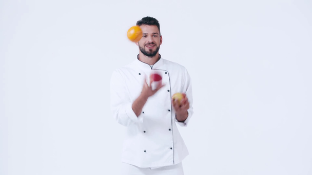 uśmiechnięty kucharz żonglujący owocami wyizolowanymi na białym - Materiał filmowy, wideo