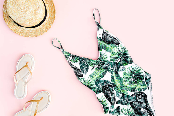 Womans beach accessories: swimsuit with tropical print, straw hat on pink background. Summer background. Flat lay - Fotó, kép