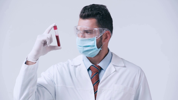 lekarz w masce medycznej patrząc na probówkę z krwią izolowaną na białym - Materiał filmowy, wideo