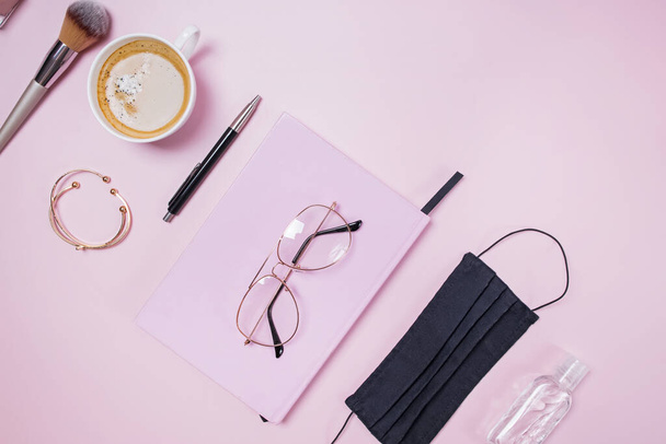 Flat lay composition with medical mask laptop, coffee, notebook on pink background. - Фото, изображение
