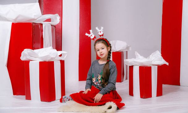 Portrait of cheerful elf kid smiling and ready to help in christmas night. wearing fantasy costume isolated over white background with red gift boxes - Photo, Image