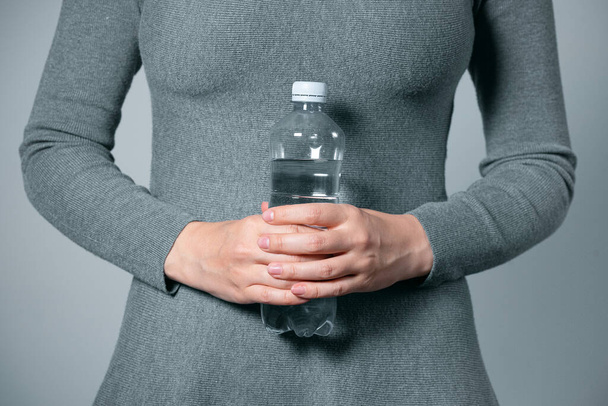 Bottle of water in female hands closeup on gray background. - Fotoğraf, Görsel