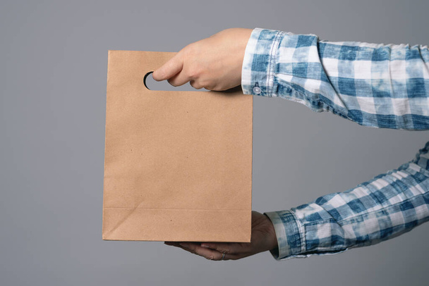 A paper shopping bag in male hand isolated on gray background. - Zdjęcie, obraz