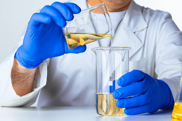 Scientist or doctor in blue gloves pouring some yellow liquid into a flask - Fotografie, Obrázek