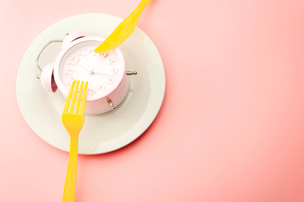 Weight loss strategy metaphor and intermittent fasting plan concept with minimal photography of clock on empty plate and vibrant yellow fork and knife isolated on vivid pink background with copy space - Foto, Bild